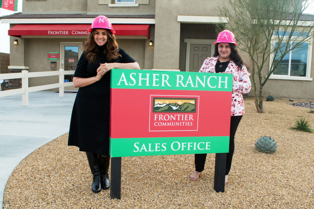 Nancy Del Salto and Adriana Zaragoza stand by Asher Ranch sign in front of new home sales center with pink helmets on