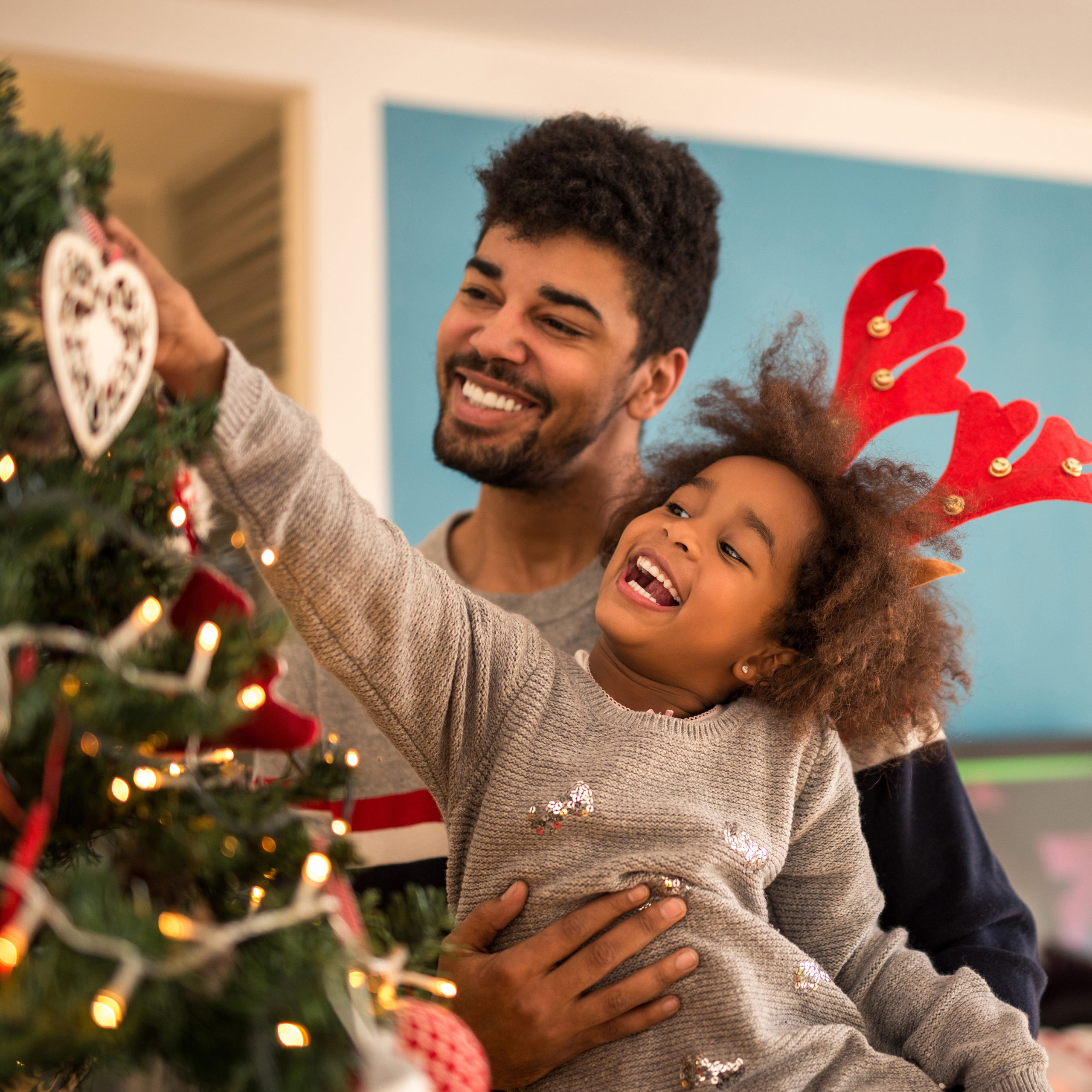 Cute african american girl decorating Christmas tree with dad.