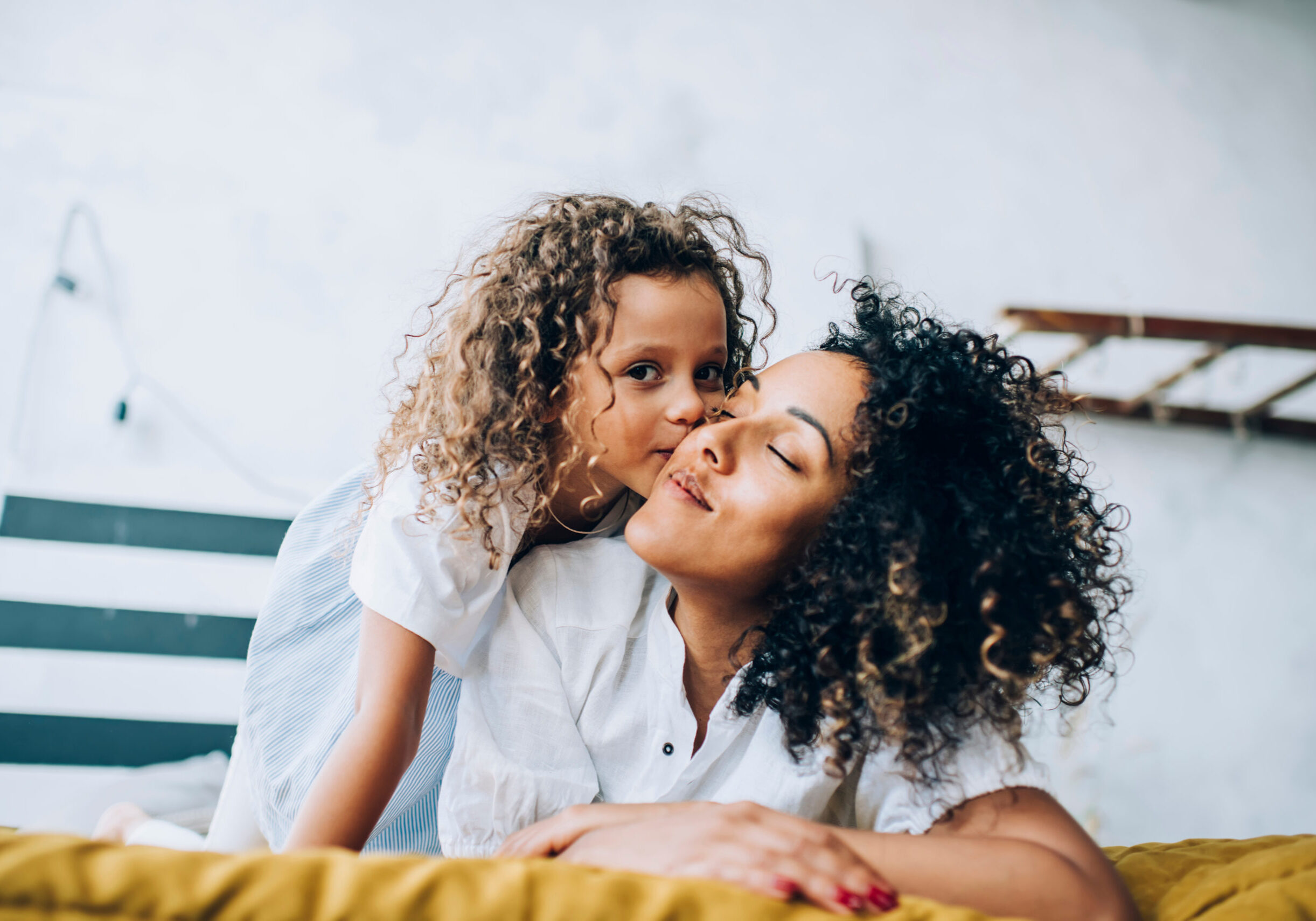 Adorable child hugging and kissing cheek of mom at home 